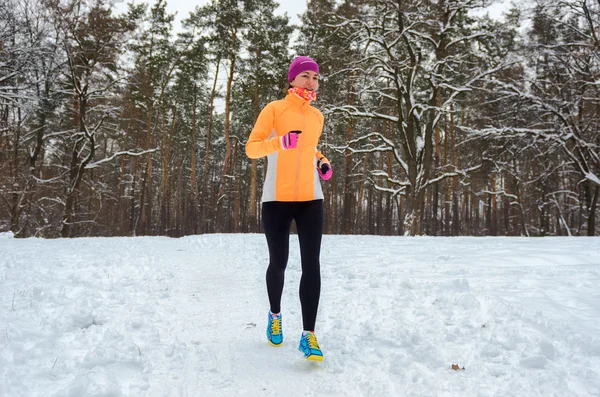 Winter running in forest: happy woman runner jogging in snow, outdoor sport and fitness concept