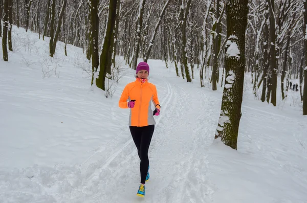 Winter running in forest: happy woman runner jogging in snow, outdoor sport and fitness concept