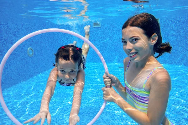 Children swim in pool underwater, happy active girls have fun under water, kids sport on family vacation
