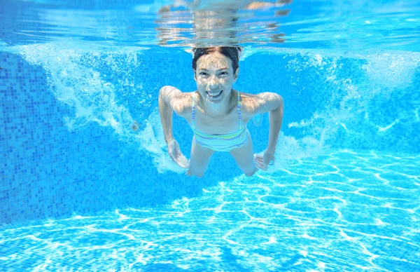 Child swims in pool underwater, happy active girl has fun under water, kid sport on family vacation