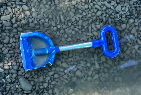 Blue shovel with pebbles in water, outdoor toy