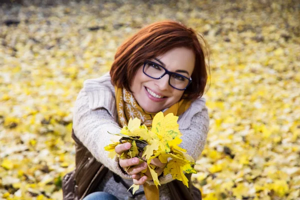 Smiling redhead woman with yellow autumn leaves