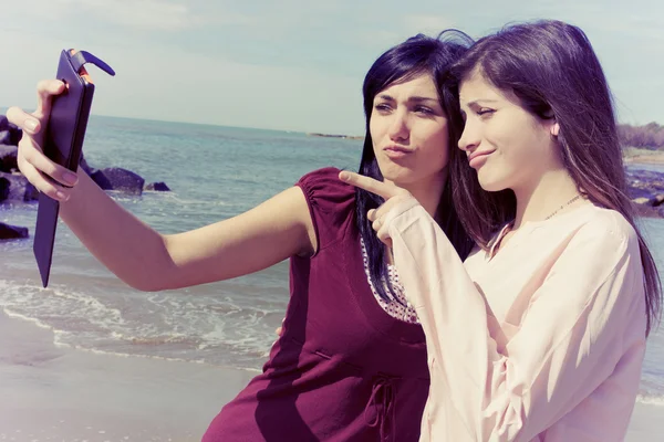 Two young women taking selfie in front of beach making funny faces vintage look