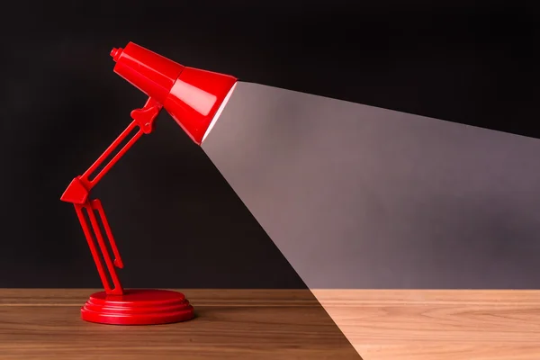 Red metal lamp on a wood desk with black background