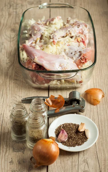 Raw rabbit meat in roaster with onion cumin and garlic on wooden vintage table