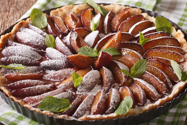 Freshly baked plum tart decorated with mint close-up. horizontal
