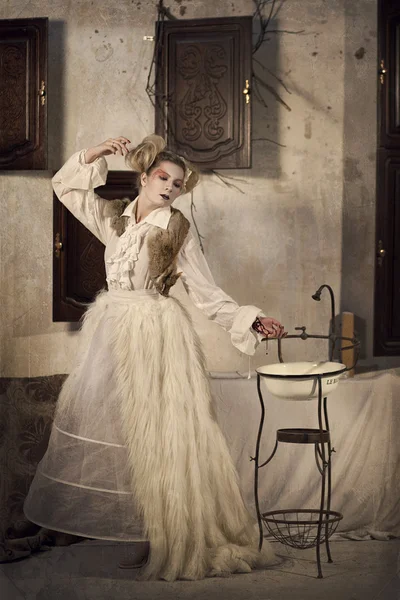 Young beautiful blonde girl in a white vintage dress, a fur cape in the form of a porcelain doll
