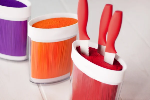 Set of knives with a red pen in the red stand standing next to the orange and purple Stands for knives