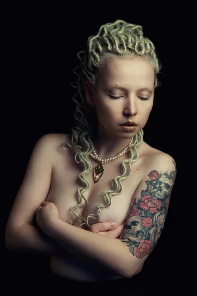 Beautiful young blonde woman with thin curly dreadlocks and a tattoo on her forearm