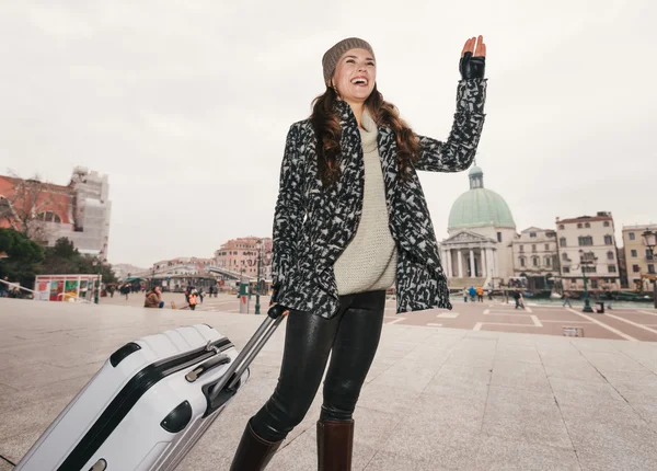 Smiling woman with big luggage bag handwaving to someone, Venice