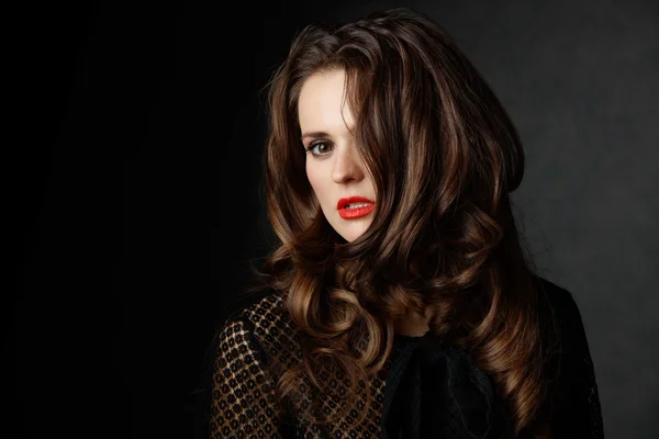 Woman with curly brown hair covering half face, dark background