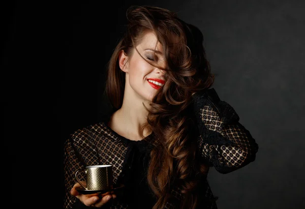 Happy woman with long wavy brown hair holding cup of coffee