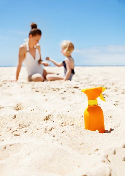 Closeup on sunscreen bottle on beach. Family in background