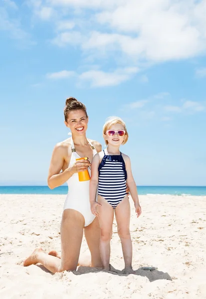 Happy mother applying sunscreen on child in swimsuit at beach
