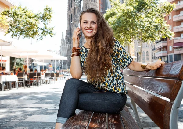 Happy woman on bench not far from Sagrada Familia talking mobile