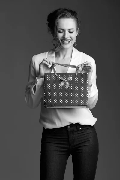 Happy woman looking inside shopping bag against grey background