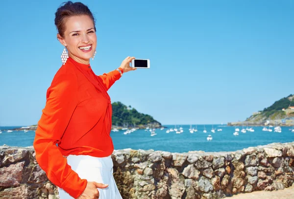 Happy woman taking photo with smartphone of lagoon with yachts