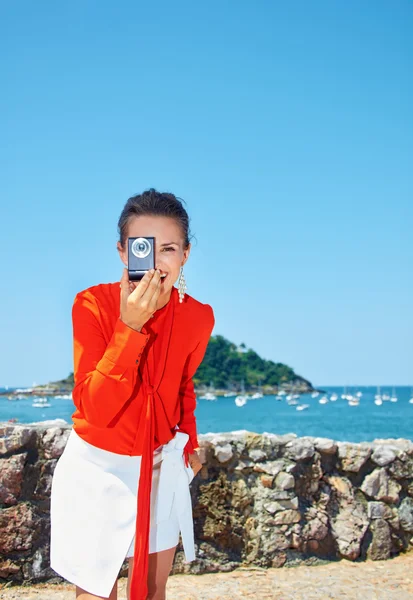 Happy woman taking photo with digital camera in front of lagoon