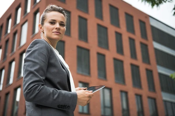 Modern business woman with tablet PC against office building