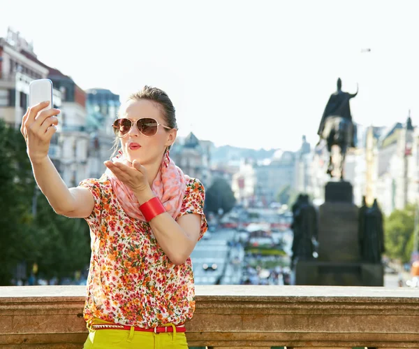 Happy young woman blowing air kiss and taking selfie in Prague