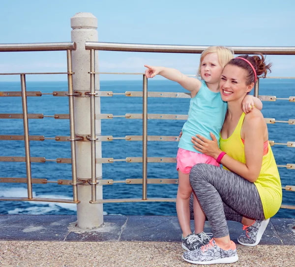 Fitness mother and child on embankment pointing on something