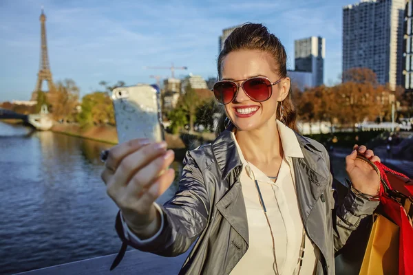 Trendy woman with shopping bag taking selfie with phone in Paris