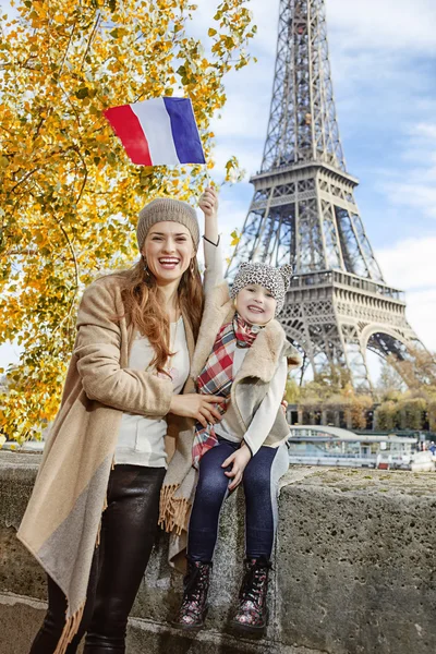 Mother and daughter rising flag while sitting on parapet, Paris