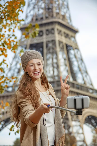 Woman taking selfie with cellphone and showing victory in Paris