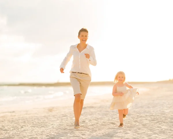 Mother and baby girl running on the beach in the evening
