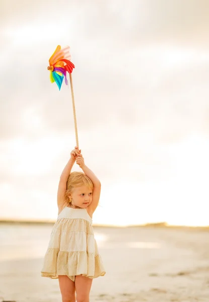 Baby girl holding colorful windmill toy on the beach in the even