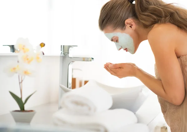 Young woman wearing facial cosmetic mask washing face
