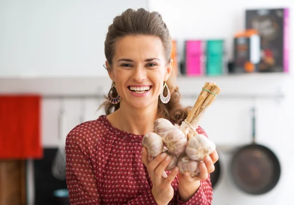Portrait of smiling young housewife showing bunch of garlic
