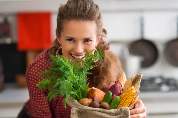 Smiling woman looking over a burlap sac of fresh fall vegetables