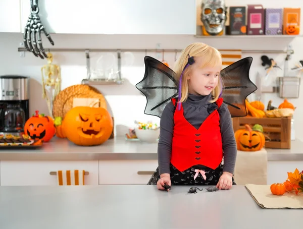 Funny girl in halloween bat costume in decorated kitchen