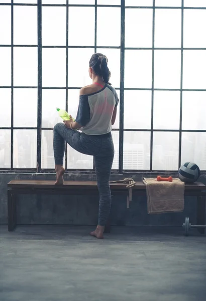 Rear view of woman looking out window holding water in loft gym