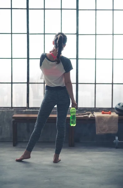 Rear view of woman in workout gear in loft gym holding water