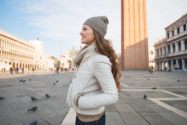 Happy young woman standing on Piazza San Marco and looking aside