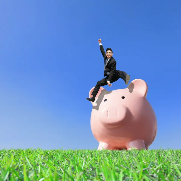 Young excited business man jump over piggy bank