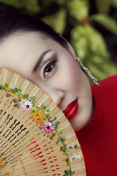 Beautiful red lip asian female hiding right half of her face behind a bamboo fan
