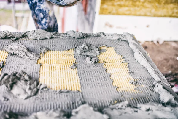 Worker applying adhesive material on insulation panel of material wool used for building facades