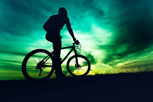 Man in helmet and protective gear on mountain bike against sunset sky