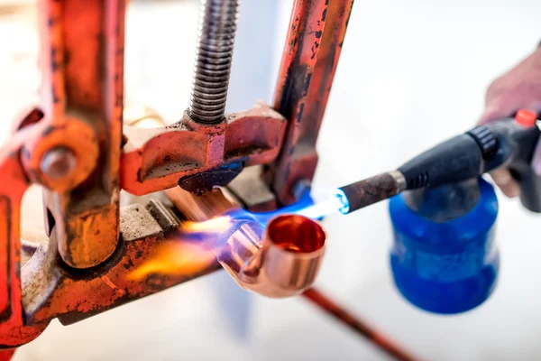 Industrial worker using propane gas torch for soldering copper pipes.