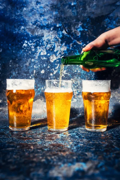 Close-up of barman hand pouring beer from bottle in beer glasses