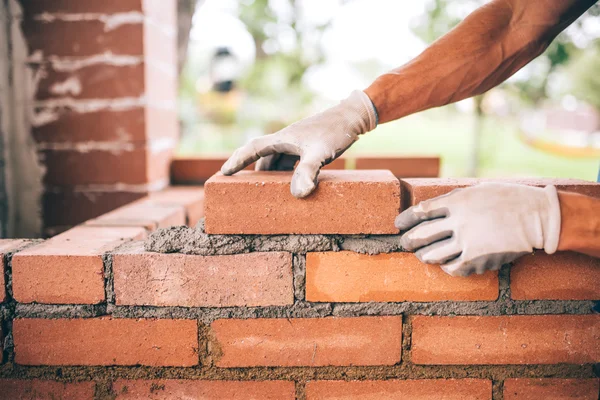 Professional construction worker laying bricks and building barbecue in industrial site. Detail of hand adjusting bricks