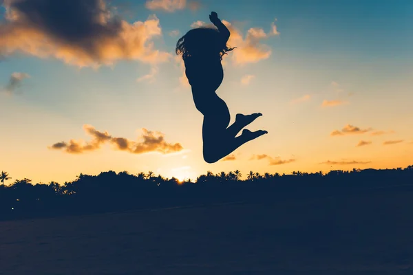 Beautiful silhouette portrait of summer girl jumping on white sand in exotic island at sunset. Serenity, relaxation, mindfulness, stress and carefree concepts.