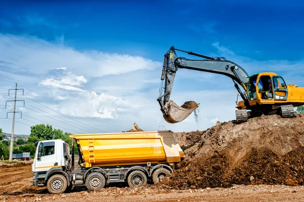 Industrial truck loader excavator and bulldozer moving earth and unloading into a dumper truck