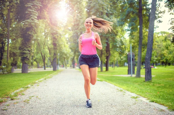 Healthy and happy woman running in urban park with headphones and music