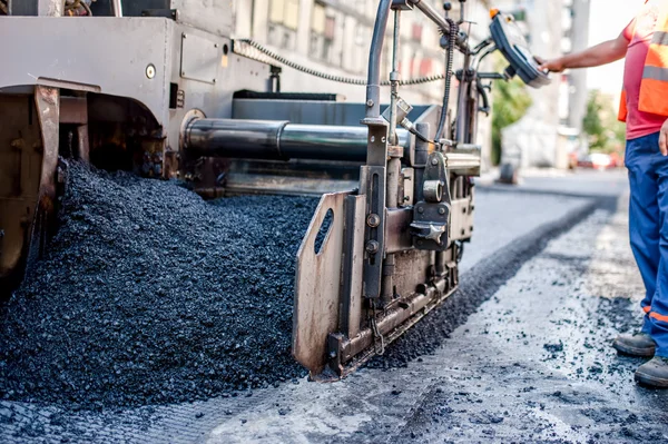 Worker or engineer operating an asphalt paving machine at road construction