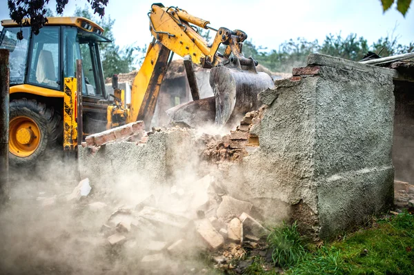 Bulldozer demolishing concrete brick walls of small building