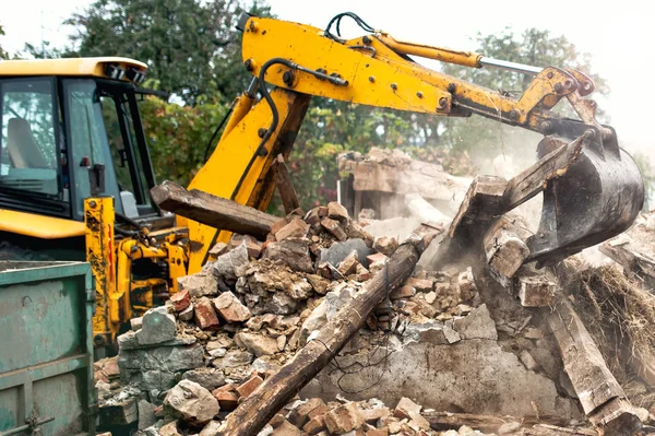 Industrial excavator and bulldozer loading debris and demolition concrete walls into a container